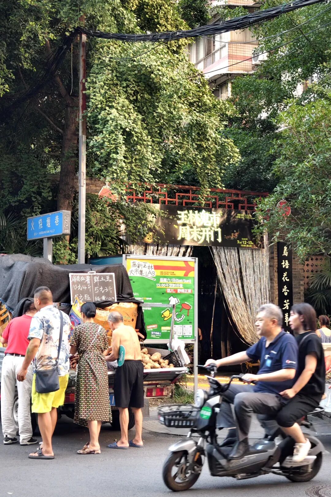 火烧堰巷入口的街头摊位、路人及骑车经过的居民