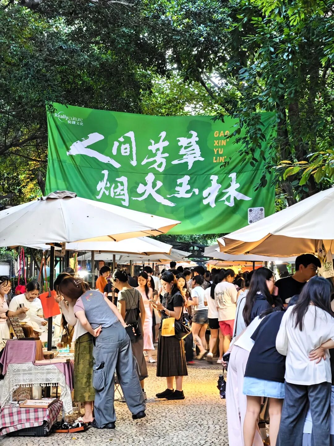绿色市集横幅下,游客在火烧堰的伞棚摊位间行走